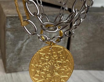 Collar con medallón dorado en capas, bicolor, tres cadenas plateadas, conectores dorados.