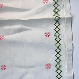 May include: White linen table runner with green and pink embroidered flowers and a border of green diamond shapes.