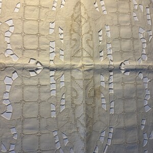 May include: A white crocheted tablecloth with a delicate floral pattern and intricate cutouts. The tablecloth has a central design with a repeating motif.