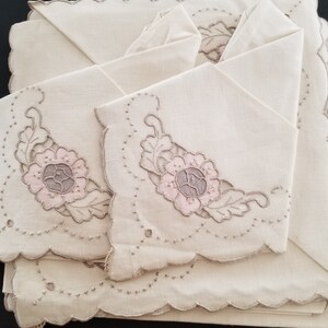 May include: Set of four off-white linen napkins with scalloped edges and embroidered floral designs in pink and gray.