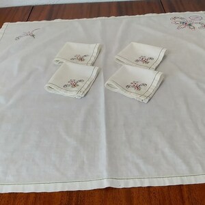 May include: White embroidered tablecloth with four matching napkins. The tablecloth and napkins feature a floral design with green, red, and blue embroidery.