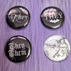 Puede incluir: Cuatro botones redondos negros y blancos con diferentes mensajes. El primer botón dice "They" en una fuente cursiva. El segundo botón dice "Excuse me, but it's THEY" con un gráfico de murciélago. El tercer botón dice "They Them" en una fuente gótica. El cuarto botón tiene una ilustración en blanco y negro de una persona con el texto "No binario".