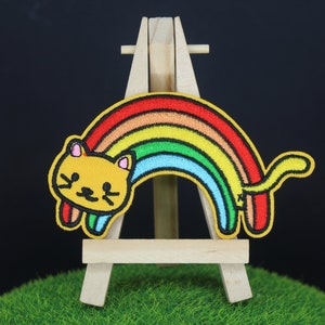 May include: A yellow cat with a rainbow arching over its back. The cat and rainbow are embroidered on a fabric patch.