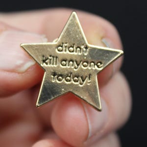Close-up of gold star enamel pin reading “didn’t kill anyone today,” shown in hand for size reference. Funny enamel badge, office humour gift, stress relief token, or quirky reward pin. Perfect for teachers, parents, or anyone needing a laugh.