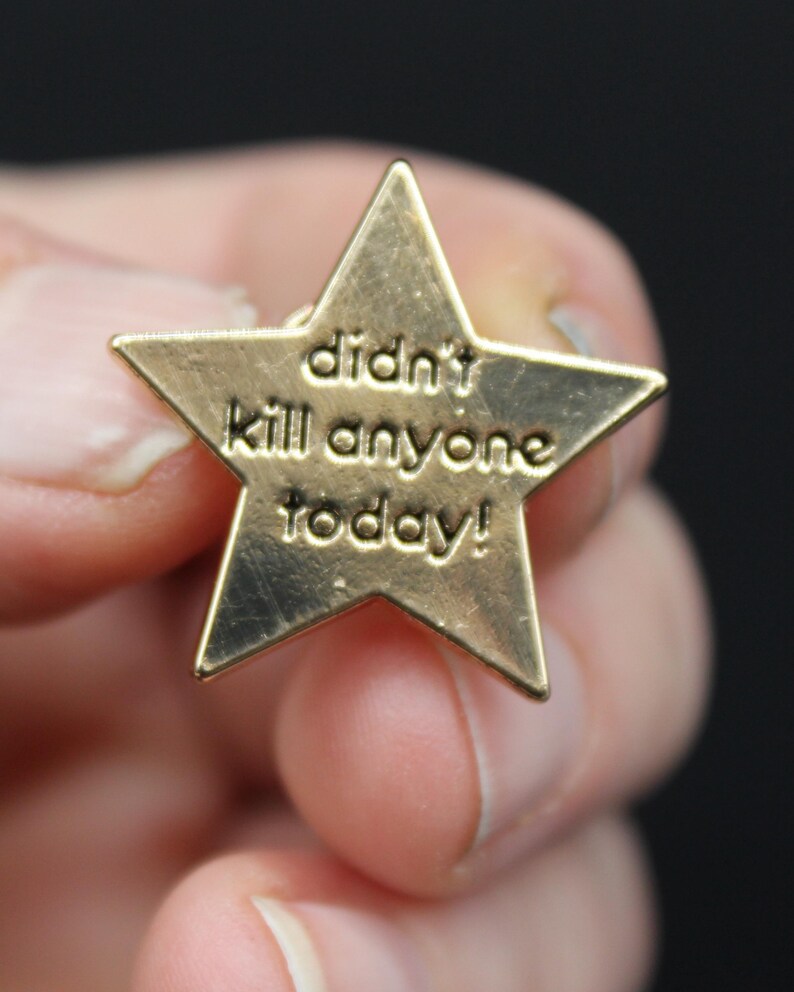 Close-up of gold star enamel pin reading “didn’t kill anyone today,” shown in hand for size reference. Funny enamel badge, office humour gift, stress relief token, or quirky reward pin. Perfect for teachers, parents, or anyone needing a laugh.