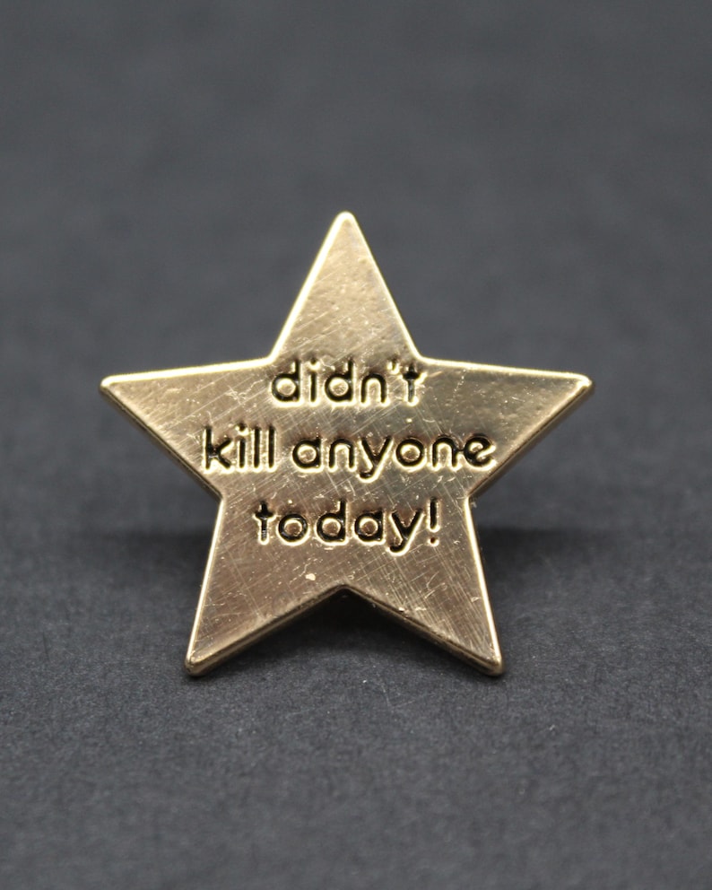 A gold star-shaped enamel pin with the words “didn’t kill anyone today!” engraved on the front. The pin has a brushed metallic finish and sits against a dark grey background, creating a playful but stylish contrast. A humorous novelty gift for adults who appreciate sarcasm and self-aware humour, ideal for workmates, friends, or anyone needing a lighthearted reminder that they made it through the day.
