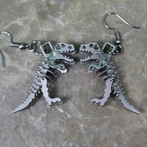 May include: A pair of silver dinosaur skeleton earrings. The earrings are dangle style with a hook fastening.