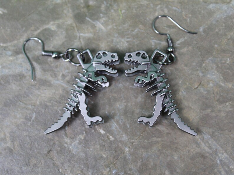May include: A pair of silver dinosaur skeleton earrings. The earrings are dangle style with a hook fastening.