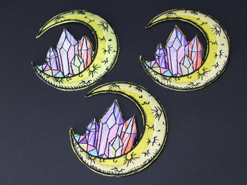 May include: Three yellow crescent moon embroidered patches with a cluster of purple, pink, and orange crystals in the center of each moon.