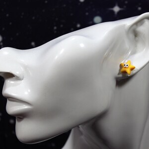 Yellow googly-eyed star earring worn on a glossy white bust, showing the fun and quirky size and fit.