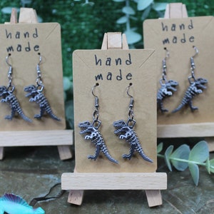 May include: Three pairs of silver dinosaur skeleton earrings on brown card stock with the text "hand made" on each card.