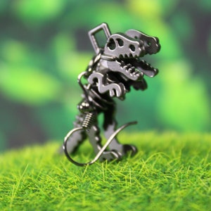 May include: Silver dinosaur skeleton earrings with a springy wire hook fastening. The earrings are on a green grassy surface.
