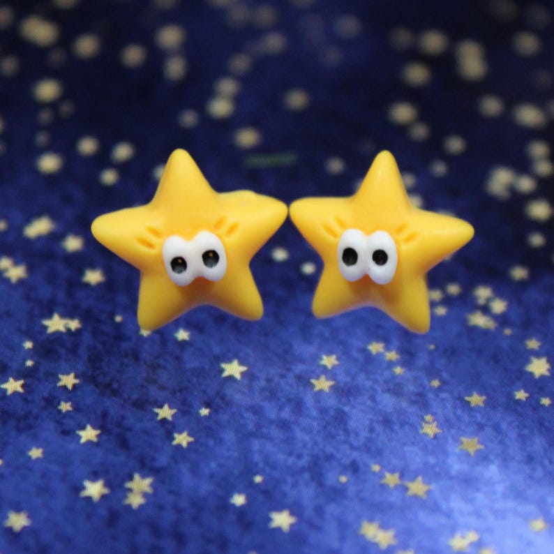 Two yellow star earrings displayed on a deep blue galaxy-themed background, evoking a dreamy space aesthetic.• Yellow star stud earrings with a playful, feel-good look
• Lightweight, comfortable for everyday wear
• Cute star shape that pairs easily with casual or dressy outfits
• A small but meaningful gift for anyone who loves Fun accessories