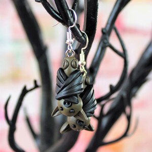 May include: A pair of dangle earrings featuring a brown and black bat design. The bats are made of polymer clay and have a realistic appearance.