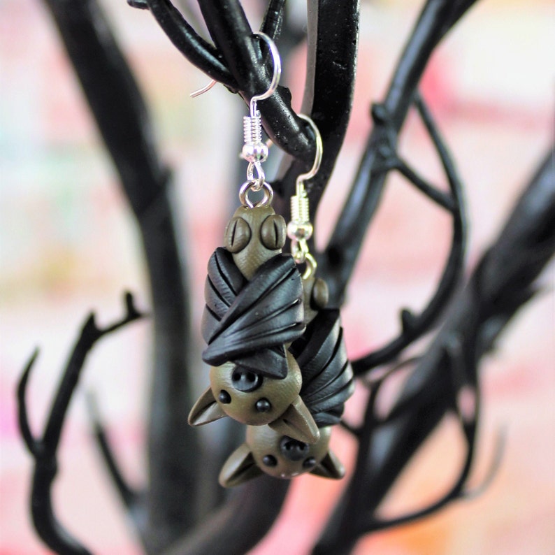 May include: A pair of dangle earrings featuring a brown and black bat design. The bats are made of polymer clay and have a realistic appearance.