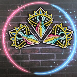 May include: Three embroidered iron-on patches with a black background and colourful details. Each patch features a stylised eye with a crescent moon and a rainbow-like design.