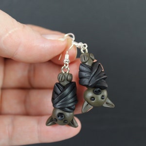 May include: A pair of dangle earrings featuring black and green clay bats with silver hooks.