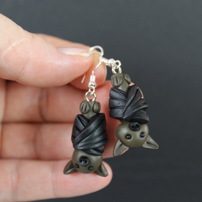 May include: A pair of dangle earrings featuring black and green clay bats with silver hooks.