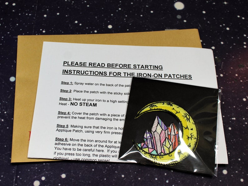May include: Instructions for applying iron-on patches. The instructions include steps for preparing the fabric, applying heat, and removing the protective backing. The image also shows a yellow crescent moon with colorful crystals inside, which is an example of an iron-on patch.