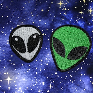May include: Two embroidered iron-on patches of alien heads. One is grey with black eyes and the other is green with black eyes.