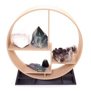 May include: A wooden circular shelf with five compartments, displaying a variety of crystals and stones. The shelf is painted a light brown color and has a black base. The crystals include a large white crystal with purple accents, a dark green crystal, a cluster of smoky quartz crystals, and a iridescent crystal.