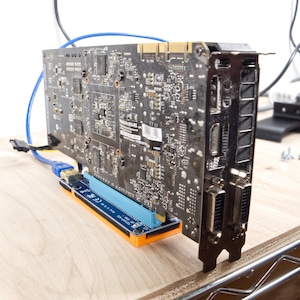 Peut inclure: Vue arrière d'une carte graphique noire avec plusieurs ports, dont HDMI et DVI. La carte est montée sur un support bleu et orange.