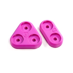 May include: Two pink plastic 3D printed parts with circular holes. One part is a triangle with three holes and the other is an oval with two holes.