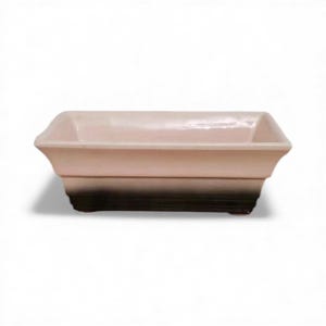 Puede incluir: Una jardinera rectangular de cerámica con la parte superior rosa claro y la base marrón oscuro. La jardinera tiene un diseño escalonado y es adecuada para plantas pequeñas o suculentas. La jardinera está sobre un fondo blanco.