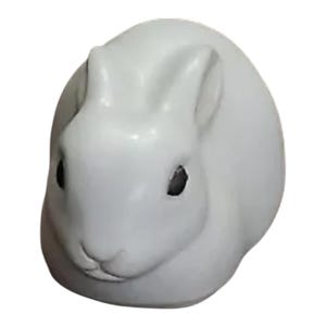 Puede incluir: Una figurita de conejo de cerámica blanca con ojos negros. El conejo está acurrucado en una posición para dormir.