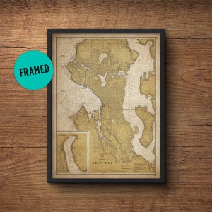 May include: A framed vintage nautical chart of Seattle, Washington. The chart is printed on aged paper with a yellowed hue and features detailed lines and markings. The title "SEATTLE" is printed in black at the bottom of the chart.