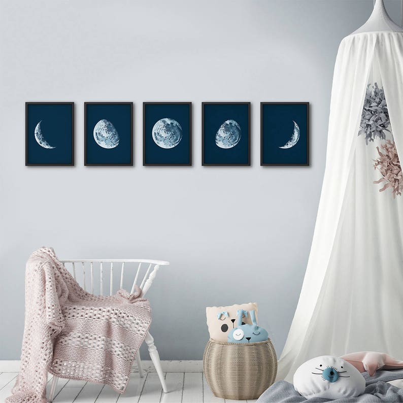 May include: Five black framed prints of the moon in different phases against a dark blue background. The prints are arranged in a row on a light blue wall.
