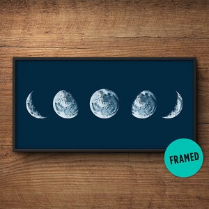 May include: A framed print of a blue watercolor moon phases design on a dark blue background. The print features five different phases of the moon, from a crescent to a full moon.