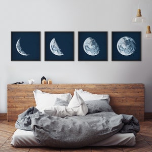 May include: Four framed prints of the moon in different phases, with a dark blue background. The prints are arranged in a row on a white wall above a wooden headboard and a bed with gray bedding.