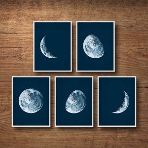 May include: Set of six blue and white moon phase prints in white frames. Each print features a different phase of the moon, from a crescent to a full moon.