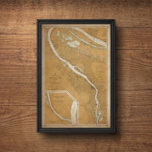 Może przedstawiać: Antyczna mapa nawigacyjna obszaru Portland, Oregon, oprawiona w czarną ramę. Mapa przedstawia rzekę Willamette i rzekę Columbia, z dokładnymi oznaczeniami głębokości, boi i innych cech nawigacyjnych.