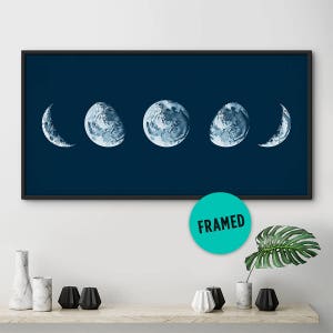 May include: A framed print of five watercolor moon phases on a dark blue background. The moon phases are in a crescent shape, half-moon shape, full moon shape, half-moon shape, and crescent shape.
