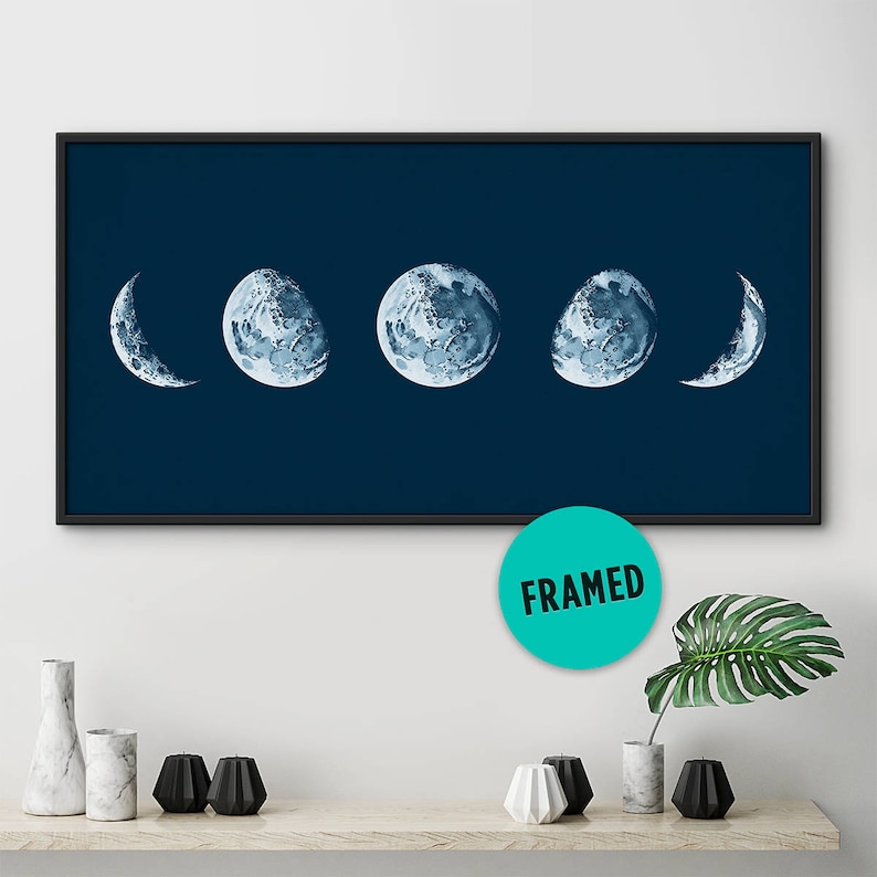 May include: A framed print of five watercolor moon phases on a dark blue background. The moon phases are in a crescent shape, half-moon shape, full moon shape, half-moon shape, and crescent shape.