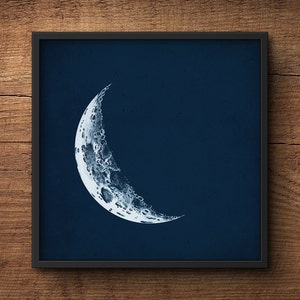 May include: A black framed print of a white crescent moon on a dark blue background.