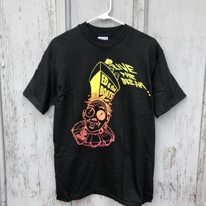 Op de afbeelding: Zwart T-shirt met een gele en oranje afbeelding van een cartoonfiguur met een hoed waarop "Live the Dream!" en "Ed & the Boats" staat.