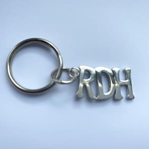 以下が含まれることがあります： 銀色のキーホルダー。銀色のリングと「RDH」と書かれたチャームが付いています。