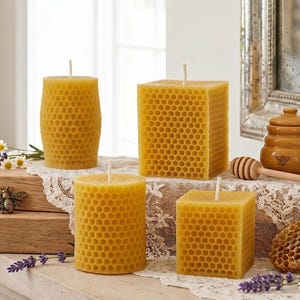 May include: Four yellow beeswax candles with a honeycomb pattern. The candles are different shapes: cylindrical, square, and rectangular. A small honey pot, dipper, and decorative bee are also visible.