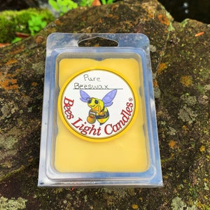 May include: A yellow beeswax candle in a clear plastic container with a label that says "Pure Beeswax" and "Bees Light Candles". The label features a cartoon bee with a bucket of honey.