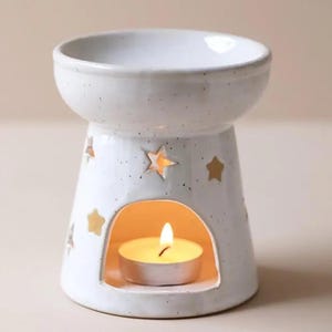 May include: White ceramic essential oil diffuser with a star design and a small tea light candle inside.