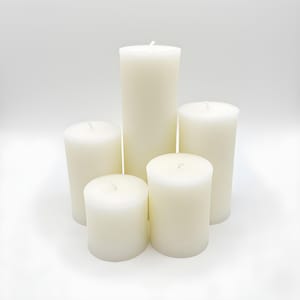 Puede incluir: Cinco velas de pilar de color marfil de diferentes alturas dispuestas sobre una superficie blanca. Las velas sin perfume tienen una forma cil&iacute;ndrica lisa. Cada vela tiene una mecha en el centro.