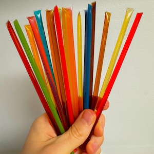 May include: A bunch of colorful, translucent, plastic drinking straws. The straws are held in a hand and are arranged in a fan shape.