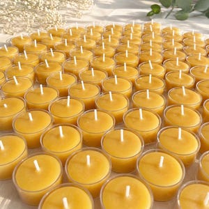 May include: A collection of yellow tea light candles in clear plastic cups. Each candle has a white wick centered in the wax. The candles are arranged closely together, creating a warm and inviting display.