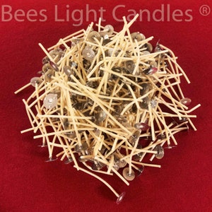 May include: A large pile of beige candle wicks with metal bases. The wicks are arranged in a random pattern on a red surface.