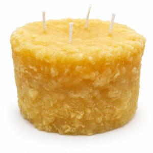 May include: A cylindrical yellow candle with a textured, granular surface and three white cotton wicks protruding from the top. The candle has a solid, opaque appearance with a consistent golden-yellow hue throughout its entire structure.