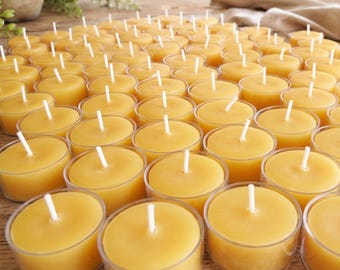 Puede incluir: Un conjunto de velas de té amarillas con mechas blancas en vasos de plástico transparente. Las velas están dispuestas juntas sobre una superficie de madera, creando un ambiente cálido y acogedor. Las velas de té son una opción popular para la decoración del hogar.