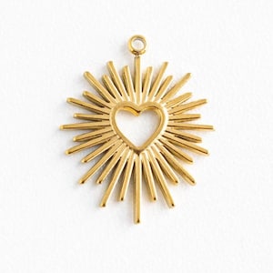 May include: Gold-toned metal charm featuring a heart shape with a sunburst design. The heart is cut out, creating a delicate openwork effect.